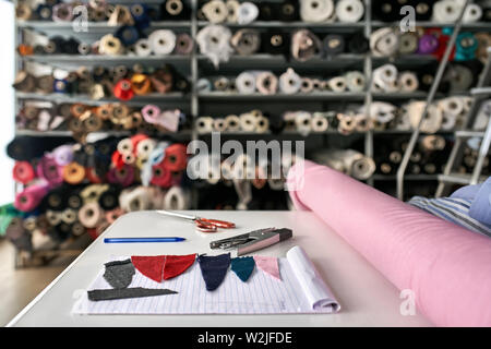 Orange scissors, stapler, blue pen, notebook with multicolored textile pieces, pink and blue textured materials are lying on the white table on the ba Stock Photo