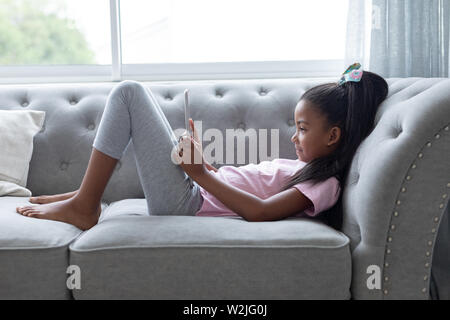 Girl using digital tablet on a sofa in living room Stock Photo