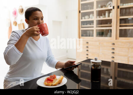 Woman using mobile phone while having coffee on a dining table Stock Photo