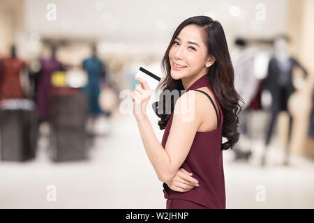 Smiling beautiful Asian women presenting credit card in hand over blurred shopping mall background, Female showing cash card for making payment to cou Stock Photo