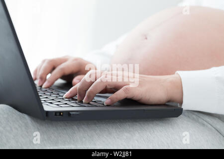 Pregnant women hand typing on keyboard on notebook to searching newborn baby items for preparing parenthood. Using a laptop computer during pregnancy Stock Photo