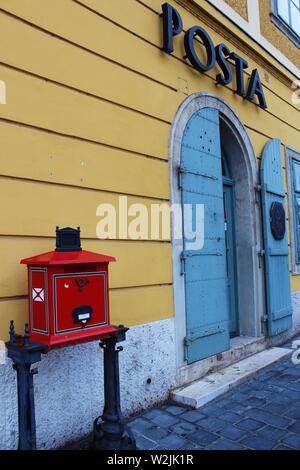 A traditional, red, freestanding postbox, on the street outside the 'Posta' (post office), in the Castle Hill district of Buda, Budapest, Hungary. Stock Photo