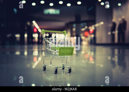 Conceptual shot of a small shopping cart put on the floor at blur background of shopping centre. Petty expenses in supermarket. Going for stuff in Stock Photo