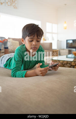 Boy playing game on mobile phone while lying on sofa at home Stock Photo