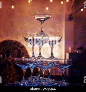 Close up of top tiers of champagne tower at the faint light of a banquet hall. Beautifull built-in set of coupe glasses at a wedding room. Wedding Stock Photo