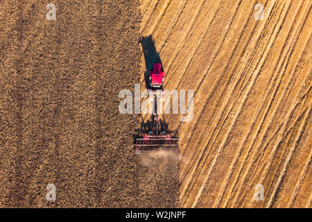 Low altitude aerial top down photo of meadow and farmer in tractor cutting the grass field after this cut grass can dry and be picked up so it can be Stock Photo
