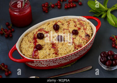 Homemade fresh cherry crumble pie with whole wheat flour in ceramic form on a dark background, ready to eat, horizontal photo Stock Photo