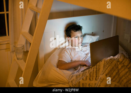 A boy using a laptop in bed at night. Stock Photo