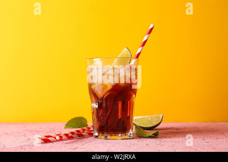 Glass with cold cola, tubule and lime slice against yellow background Stock Photo