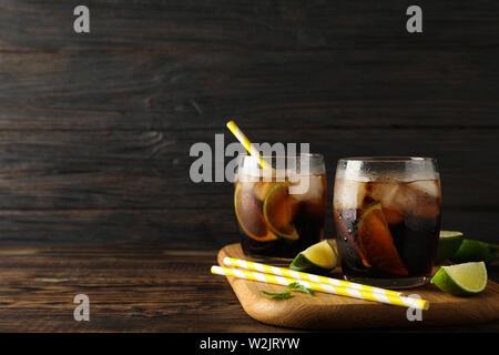 Glasses with ice cola, lime slices and tubules on wooden background Stock Photo