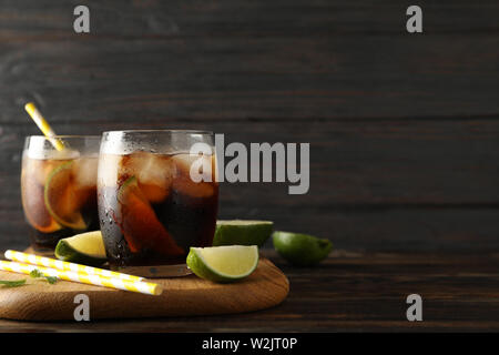 Glasses with ice cola, lime slices and tubules on wooden background Stock Photo
