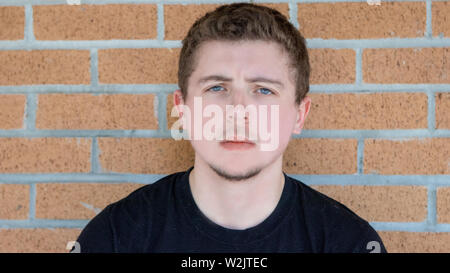 A pretty young man with pale skin short curly hair and bright blue eyes looks into the camera with a slightly mad and confused face. Stock Photo