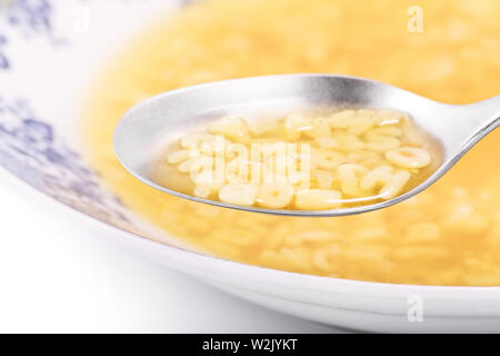 A close up shot of a spoon with alphabet noodles and a bowl full of warm alphabet soup. Stock Photo