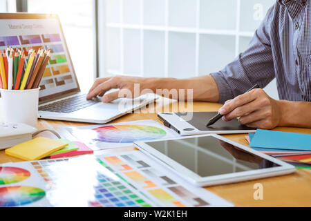 Young creative graphic designer working on project architectural drawing and color swatches, selection coloring on graphic chart with work tools and e Stock Photo