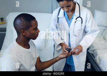 Female doctor taking patients blood sample with lancet pen in the ward Stock Photo