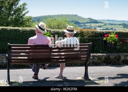 Elderly retired couple relaxing on a park bench taking in the view of Blackmore Vale in shaftesbury, Dorset Stock Photo