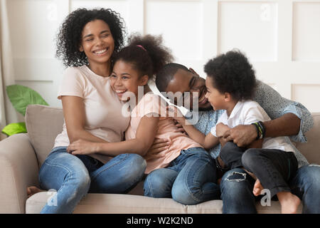 Happy african american family of four laughing bonding on sofa Stock Photo