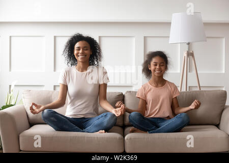 Happy african mom teaching kid daughter doing yoga at home Stock Photo