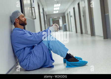 Tensed male surgeon sitting in the corridor Stock Photo