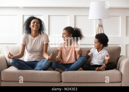 Happy laughing single black mom meditating with kids at home Stock Photo