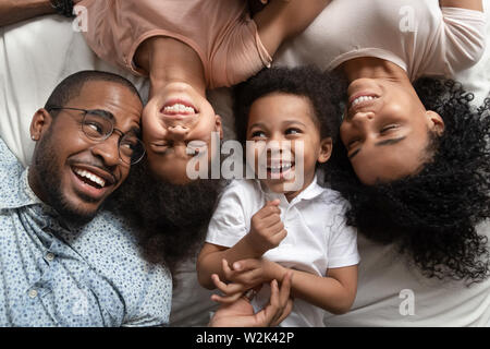 Funny affectionate african parents and kids laughing lying on bed Stock Photo