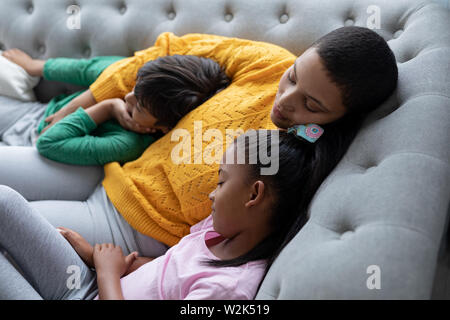 Mother and children sleeping together on a sofa in living room Stock Photo