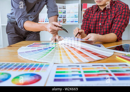 Teamwork of young creative designers working on project together and choose color swatch samples for selection coloring on digital graphic tablet at w Stock Photo
