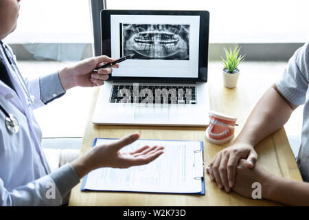 Image of doctor or dentist presenting with tooth x-ray film recommend patient in the treatment of dental and dentistry, working at workplace. Stock Photo