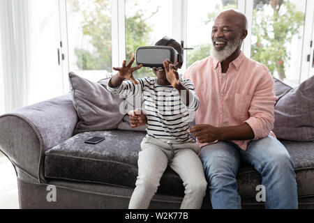 Grandson with grandfather using virtual reality headset in living room Stock Photo