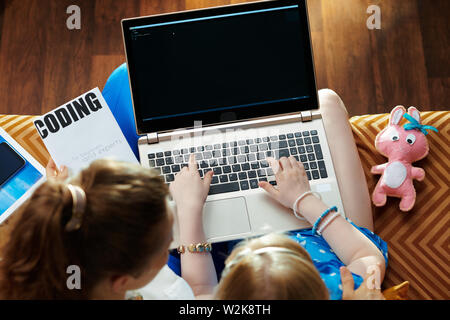 modern mother and child sitting on couch in the modern living room learning writing code in editor on a laptop. Stock Photo
