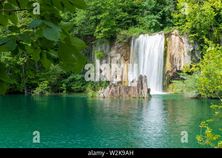 Crystal clear, pure water rushing down mossy rocks into a beautiful azure colored lake at the Plitvice Lakes National Park in Croatia Stock Photo