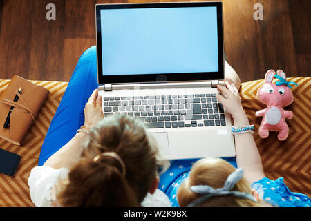 modern mother and daughter sitting on sofa in the modern living room looking at blank screen on a laptop. Stock Photo