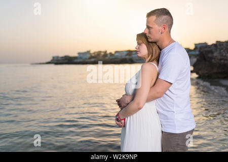 Pregnant woman embracing with her husband on the beach at sunset Stock Photo