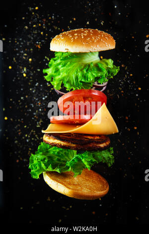 Flying ingredients for a homemade burger on a black background. Not diet food, unhealthy food. Stock Photo