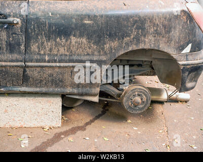 A car wreck built on stones in former dark blue or black, the wheels are dismantled, the paint dirty, scratched body full of damage. Stock Photo