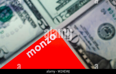 Monzo Bank cards on a blurred background of dollar bills different denominations. Stock Photo