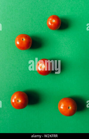 Five cherry tomatoes on a green background. Stock Photo