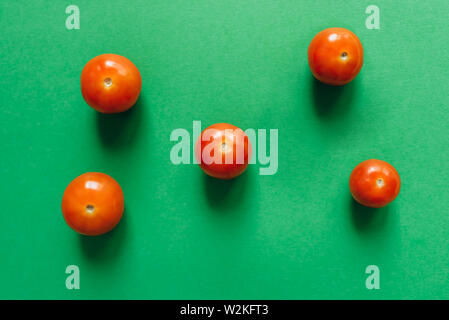Five cherry tomatoes on a green background. Stock Photo