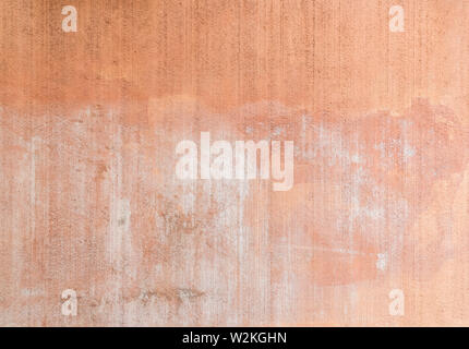 Plastered, painted, weathered, rough and red, orange or peachy concrete or stone wall with marks as a result of graffiti removal. Copy space. Stock Photo