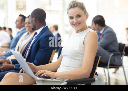 Young Caucasian female executive using laptop in conference room, smiling to camera Stock Photo