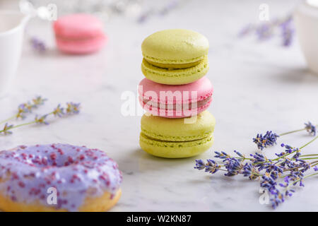 Three macarons and sprigs lavender in center of image, one lilac donut in front, one macaron behind, on white marble table Stock Photo