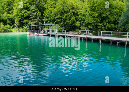 View of one of the ferries operating at the Plitvice Lakes National Park moored to the pier at the shore of Lake Kozjak and charging batteries Stock Photo