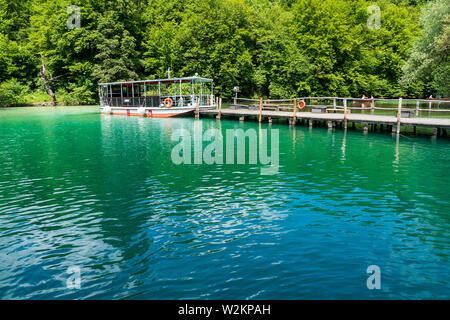 View of one of the ferries operating at the Plitvice Lakes National Park moored to the pier at the shore of Lake Kozjak and charging batteries Stock Photo