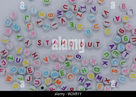 Stand Out, spelt out in red letters, surrounded by a sea of random letters, on a white background.  Creative concept : dare to be different Stock Photo