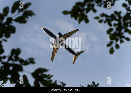 A Ryanair Boeing 737-800 airliner is seen flying high above trees near to Manchester Airport, UK. Stock Photo