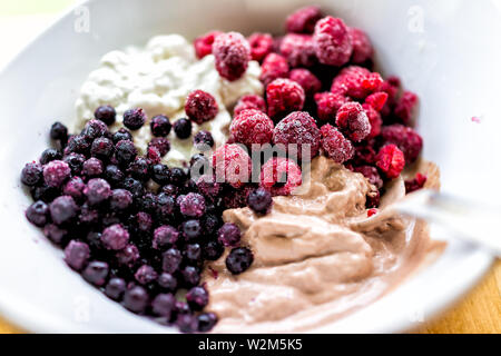 Macro closeup of colorful bowl of vanilla and chocolate ice cream topped with frozen blueberries bilberries and red raspberries berries Stock Photo