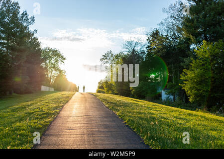 Sugarland Run Stream Valley Trail hike in Herndon, Virginia, Fairfax county in spring with paved path road and silhouette of couple walking Stock Photo