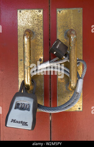 A doorway is secured with heavy metal cable land multiple locks Stock Photo