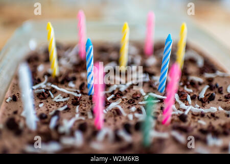 Closeup macro view of homemade chocolate raw vegan coconut cake with cacao nibs beans with colorful pink blue ad yellow birthday candles Stock Photo