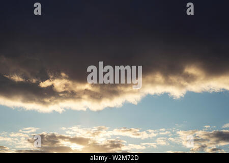 The sky is full of dark clouds in bad weather before a big storm rain. Big black gloomy rain cloud in the sky over the cloudless blue sky . Stock Photo